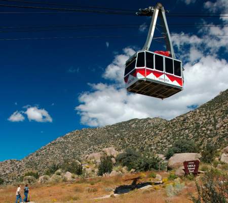 A couple hiking looks up at the Sandia Peak Aerial Tramway overhead