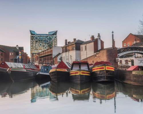 Canal boats moored at Gas Street Basin Birmingham in front of bring building a a large cubed glass building behind