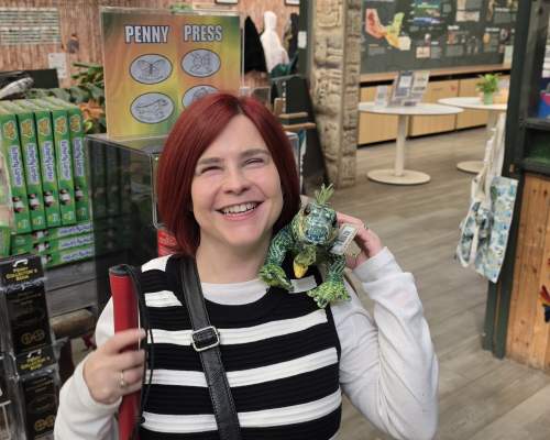 Sassy in the Butterfly Farm gift shop, she has a stuffed iguana on her shoulder smiling towards the camera