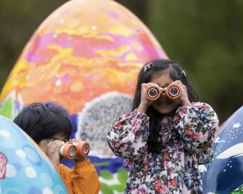 children in puddlesuits looking through binoculars, huge easter eggs in the background