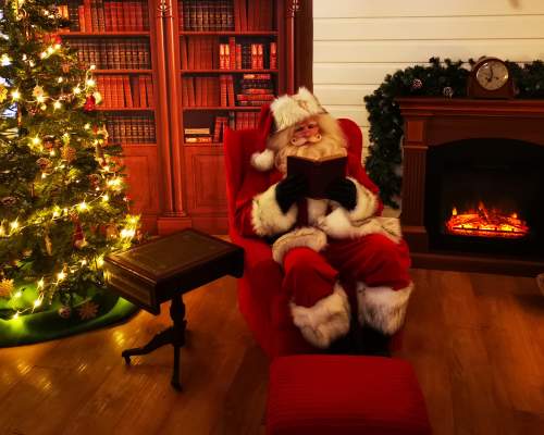 father christmas sitting in an armchair reading a book next to christmas tree