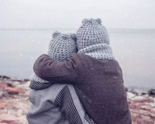 two children in hats having a hug on a wintery beach