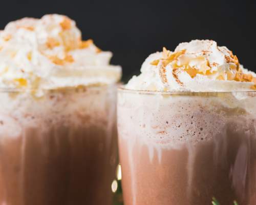 A close up of two hot chocolates in glass mugs, topped with lashings of cream.
