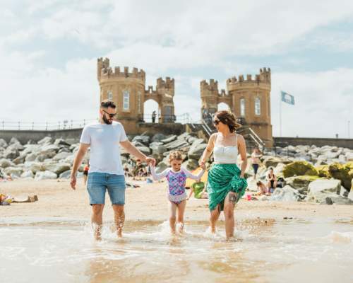 a family paddling in the sea at Withernsea Beach with the pier towers in the background.