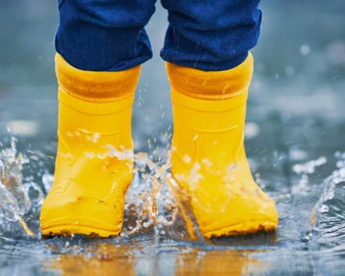 A child wearing yellow wellies jumping in a puddle
