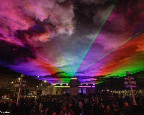 Lightport at Monument Square in Southport, image shows rainbow coloured lasers over a crowded Monument Square