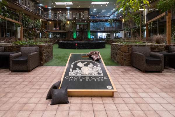 atrium of the cactus cove inn and suites. green putt putt area surrounding a black fountain and string lights above and a corn hole board with a cactus logo in the foreground