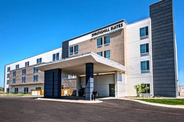 the exterior of springhill suites by marriott in amarillo features a modern four story hotel with a covered drive up entrance, clean lines, and neutral tones set against a bright west texas sky.