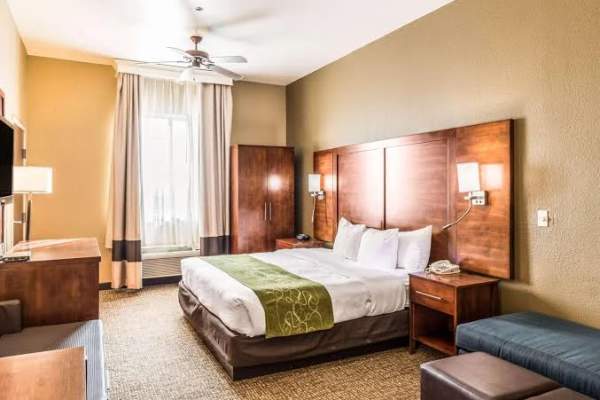 a warm and inviting Amarillo hotel room with a king bed, crisp white linens, and wood accents, featuring a cozy seating area, soft lighting, and a window letting in natural West Texas light