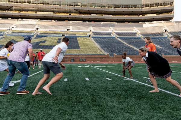 Group of people running football play on field at Michigan Stadium
