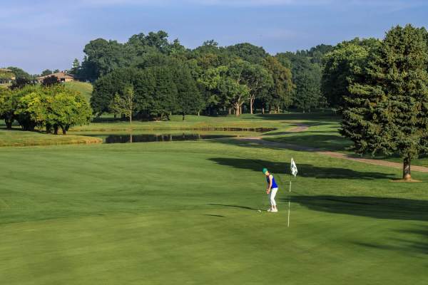 Woman sets up ready to putt on a golf course. Full, green trees fill the background.