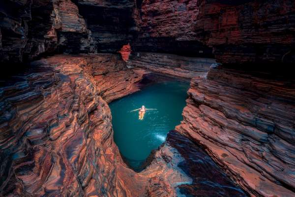 A woman floats in the emerald waters of Kermits Pool, with the walls of Hancock Gorge towering above her.