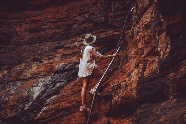 A woman climbs rocks using the handrail at Handrail Pool in Weano Gorge, Karijini National Park