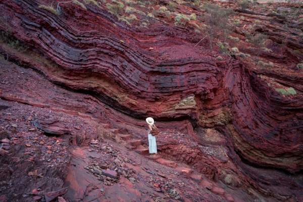 A woman pauses on the steps into Hamersley Gorge to view theancient rock formations, seen as swirling bands of red and grey