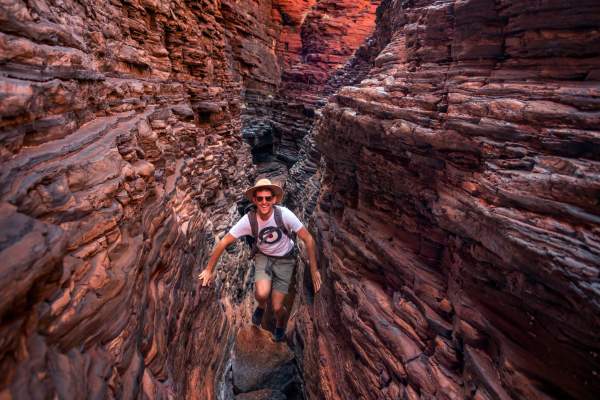 A man looks towards the camera as he traverses Spiderwalk in Karijini National Park, using his hands and feet along narrow rock ledges.
