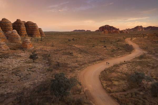 Two people walking on a track near the Bungle Bungle domes at sunset.