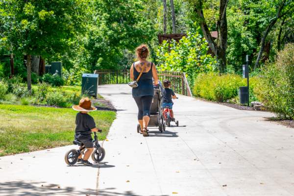 Sunny day on a paved trail with a mom pushing a stroller and kids riding bikes.