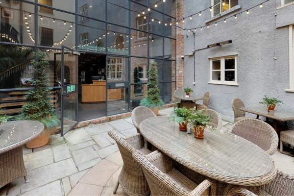 An ourdoor patio with tables and chairs in front of a large glass windows and doors - Credit Hotel Du Vin