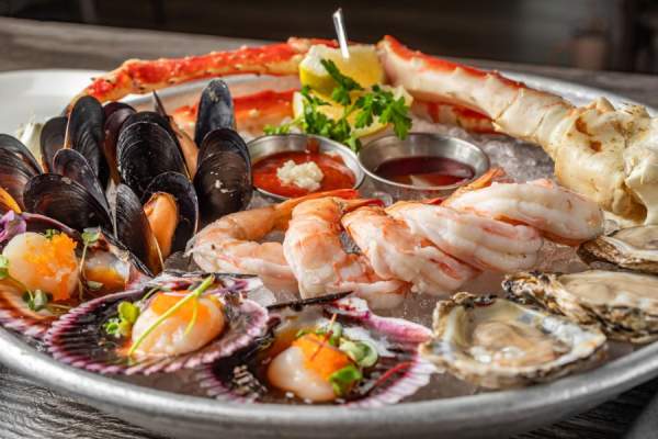Plate with oysters, clams, shrimp and crab legs with dipping sauce and lemon wedges.