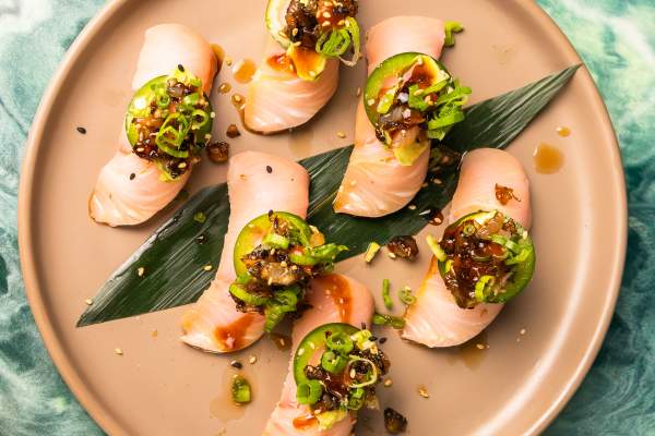6 raw slices of fish on a plate with seaweed, each with a slice of jalapeno pepper and garnish on top.