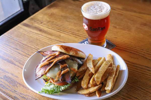 Bacon burger on a plate with wedge fries and a SanTan Brewing glass filled with beer.
