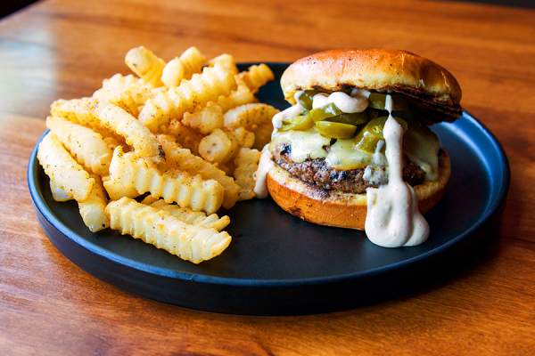 Burger with jalapenos and crinkle-cut fries on a black plate.