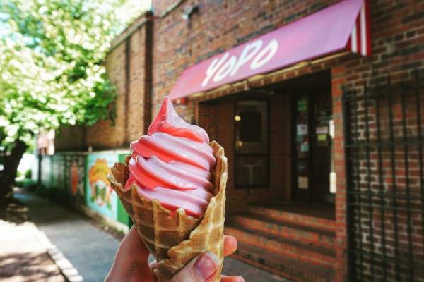 Person holding yogurt ice cream cone in front of yogurt shop