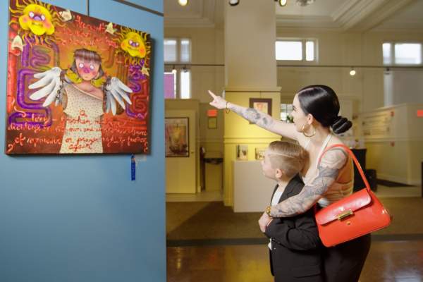 Adult and child viewing a colorful art exhibit inside a local arts center, with the adult pointing at the artwork on display.