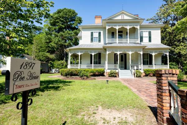 Front view of the historic 1897 Poe House in Fayetteville, North Carolina, surrounded by greenery and featuring its signature wraparound porch and ornate trim.
