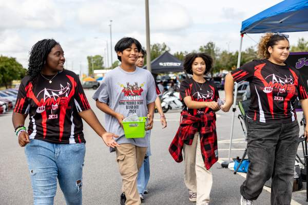 Teens and tweens walk together in matching marching band shirts at an outdoor event in Cumberland County, NC, smiling and chatting in the sunshine.