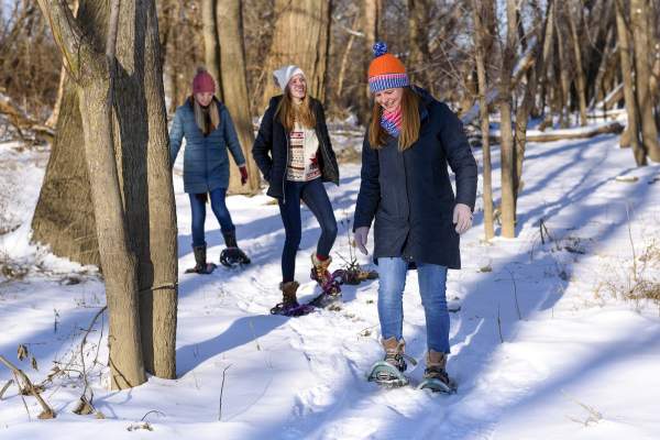 girls wearing snowshoes walking through the snow