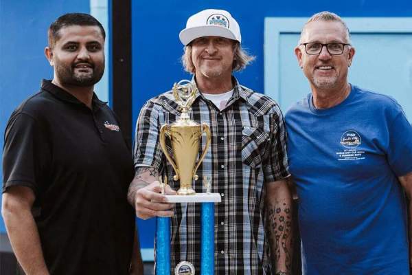 3 men smiling, with Best in Show award held by man in the center