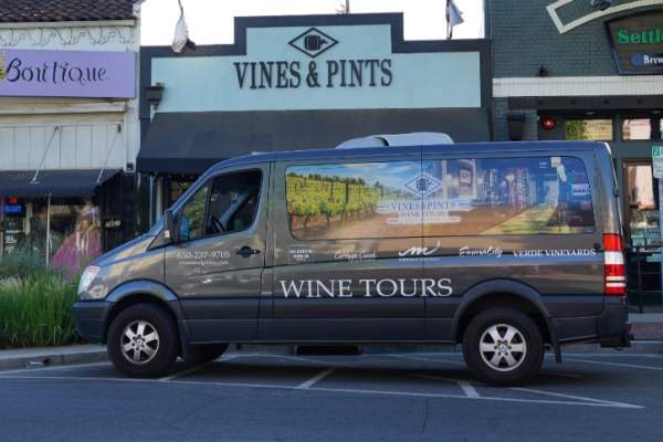Vines and Pints Wine Tours van parked in front of their downtown business storefront.