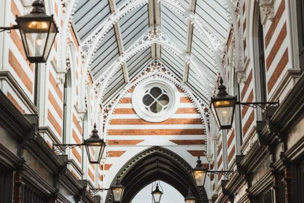 The ceilings of Paragon Arcade with the sun shining through on a clear day. The arches are supported with striped brick and lined with Victorian lamps leading to the shops and cafes below.