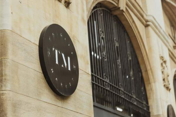 The sign for Trinity Market. The black arched entrance is to the right. The sign is black with a white "TM" in the centre in a sleek font. "Trinty Market" curves around the cirular edge of the sign.