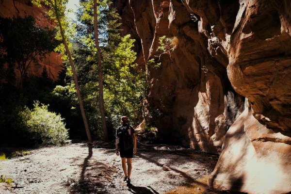 A man hikes through a red rock slot canyon in Southern Utah