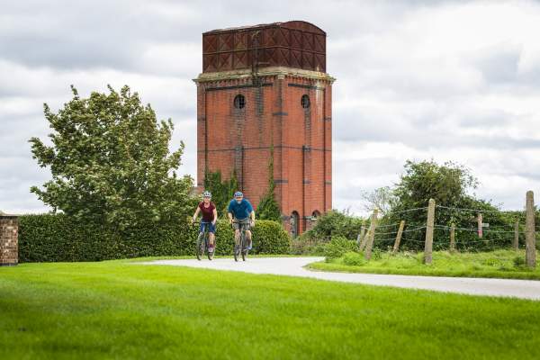 Two people cycling through the countryside and past a tower in Bardney