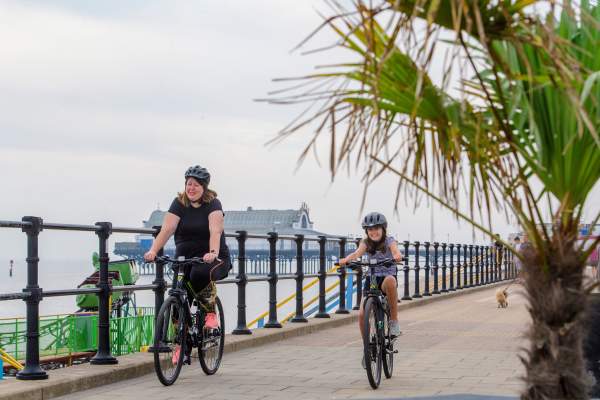 Mother and daughter cycling near the seafront with a pier in the background