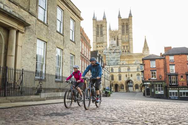 A man and woman cycling in front of Lincoln Cathedral