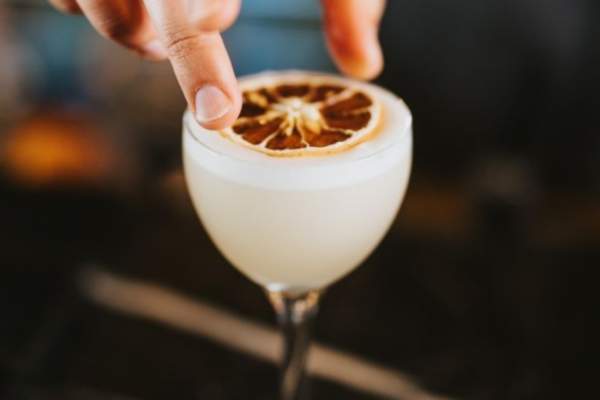 A pino colada white cocktail with a bartender putting dried fruit on top