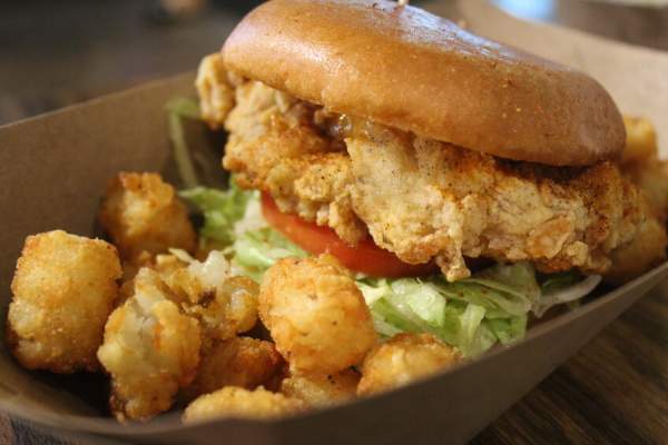 Fried chicken sandwich with lettuce and tomato and a side of tater tots
