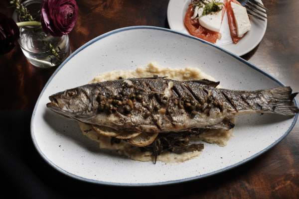 An overhead shot of a plate with a whole fish cooked with lemon and capers