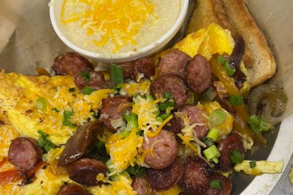 Omelet on a plate with sausage, cheese, green onions, toast and grits topped with cheese