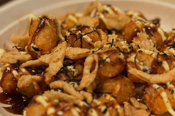 A bowl of tater tots covered in toppings and sauce
