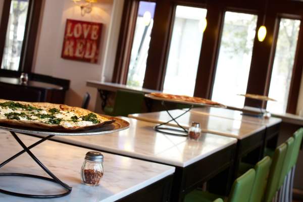A long table holds two pizzas on elevated trays