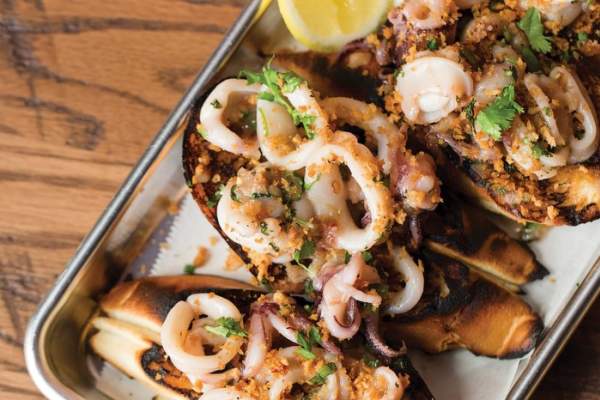 Fried squid rings on top of toast served on a rectangle platter with lemon