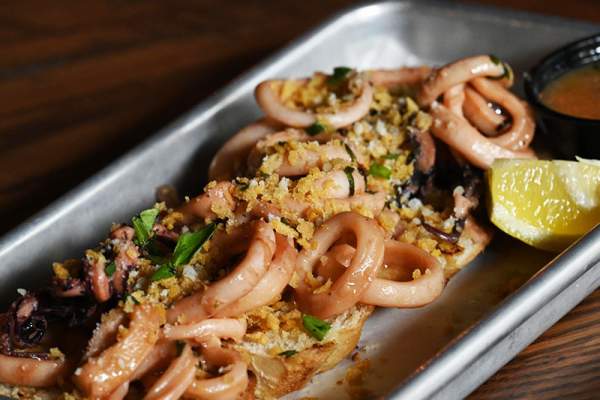 Squid Ink Seafood Pasta on a silver tray with lemon wedge