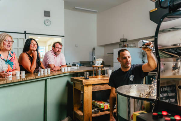 Elio roasting coffee as experience attendees view from the counter and sip on coffee