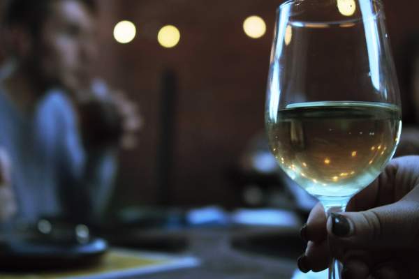 Glass of white wine with person sitting in the background.