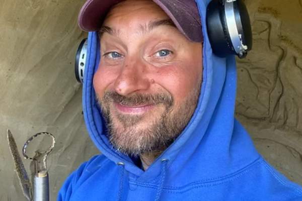 Smiling portrait of Nikolai Torkhov wearing a blue hoodie and a baseball cap outdoors.